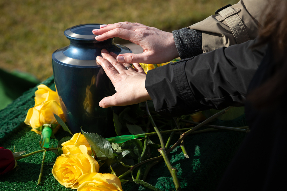 Hands,touching,a,burial,urn,in,a,bright,outdoor,funeral